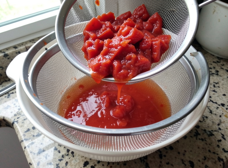 Pizza sauce being drained through a fine sieve to remove excess watery liquid