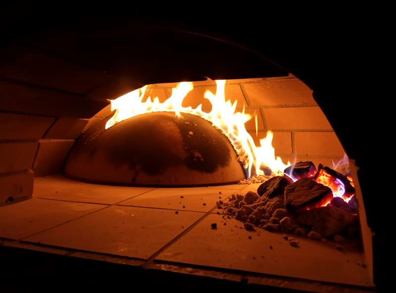 A wood-fired pizza oven with a live flame next to a gas pizza oven for comparison