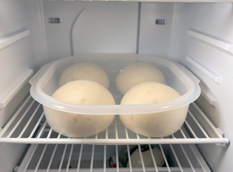 A polypropylene dough proofing tray with a translucent lid holding four round dough balls in a fridge