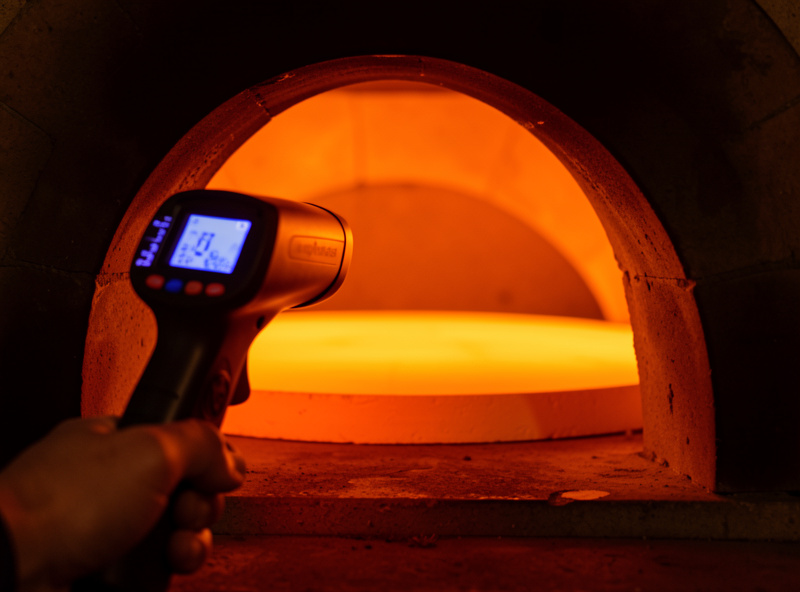 Infrared thermometer pointed at a glowing pizza oven stone showing a surface temperature reading