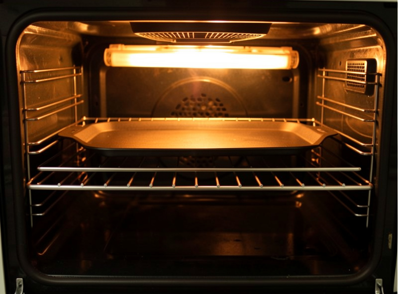 A pizza steel on the top rack of a home oven directly under a glowing broiler element